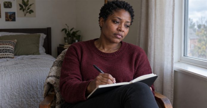 Woman writing an emotional check-in in a notebook beside a bedroom window.